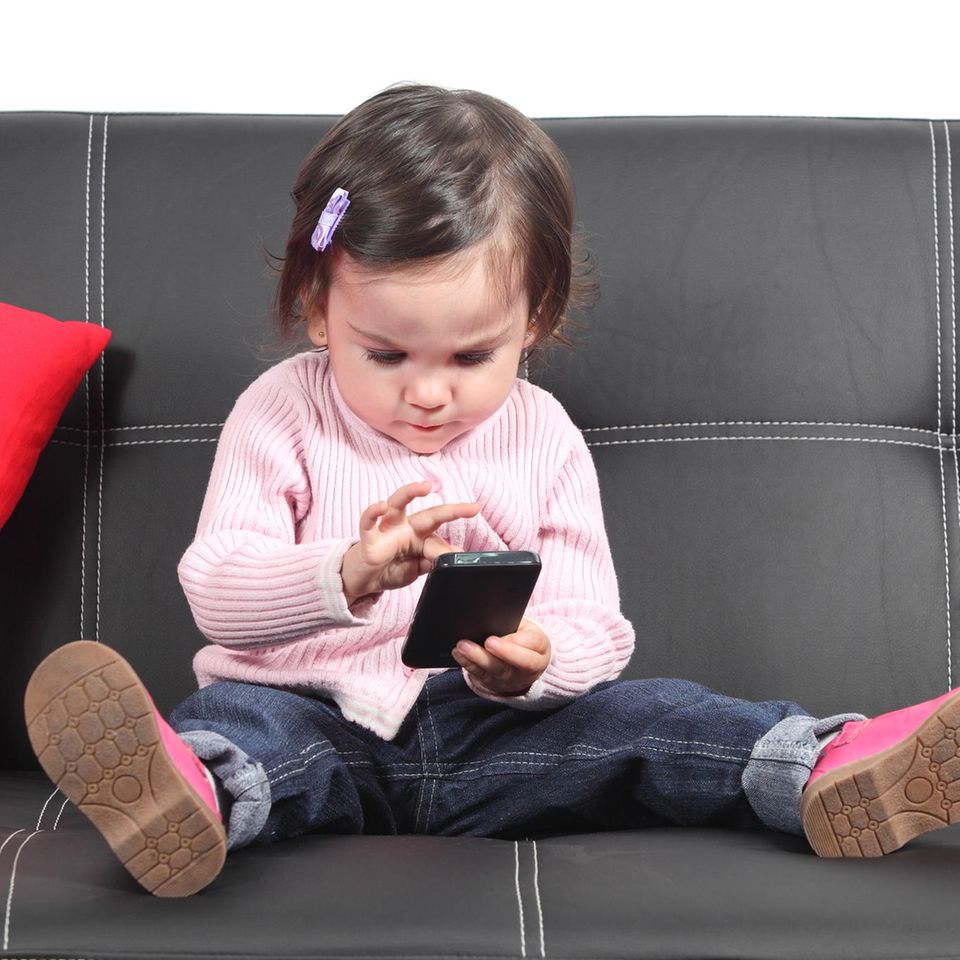 #meinkindtwittert: Kleinkind mit Handy auf einem schwarzen Sofa