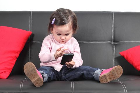 #meinkindtwittert: Kleinkind mit Handy auf einem schwarzen Sofa