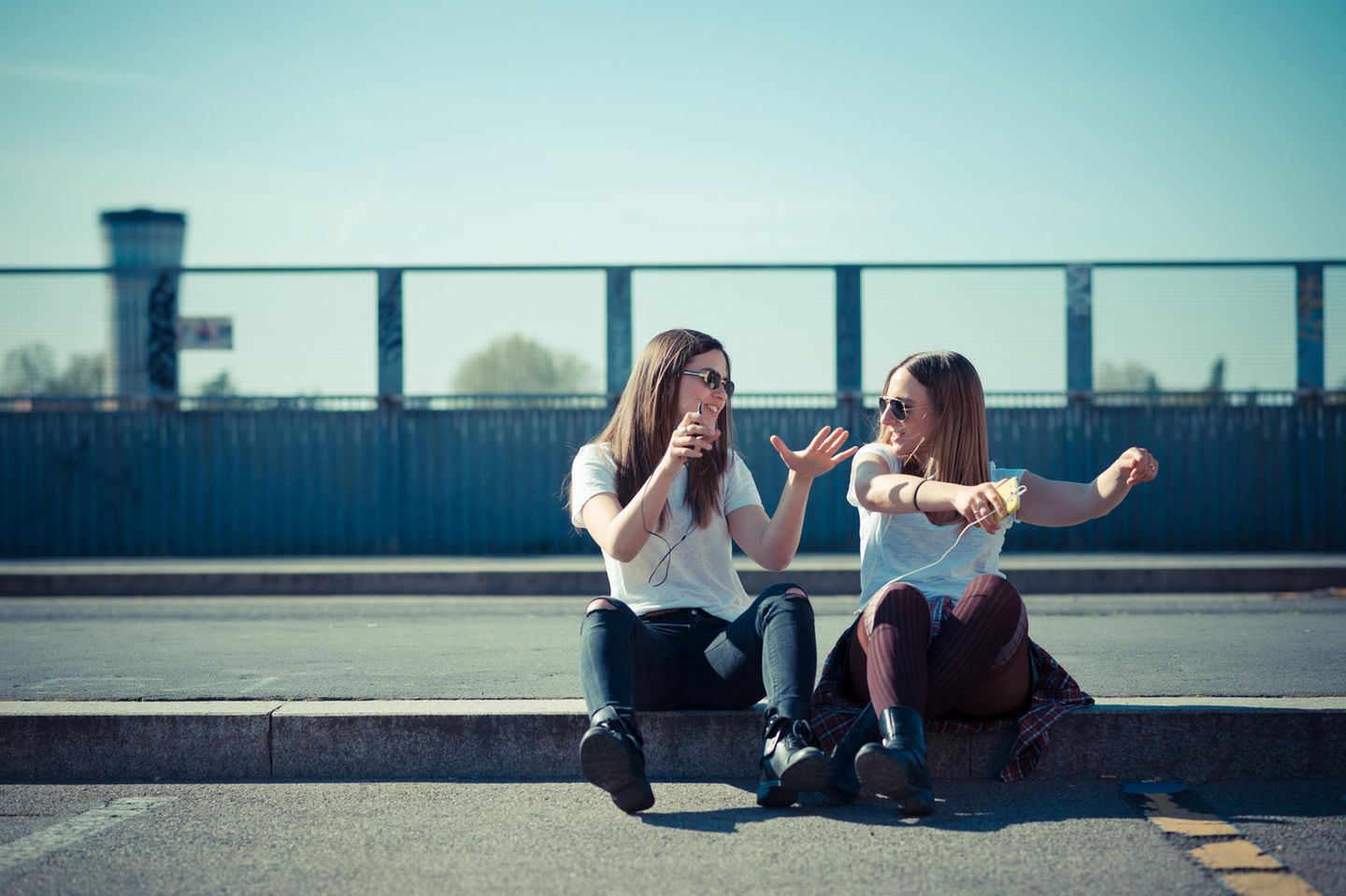 PSychologie: Zwei Freundinnen sitzen auf dem Bürgersteig und tanzen