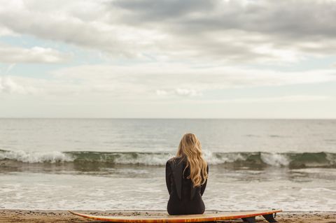 Psychologie: Eine Frau sitzt am Strand auf einem Surfbrett