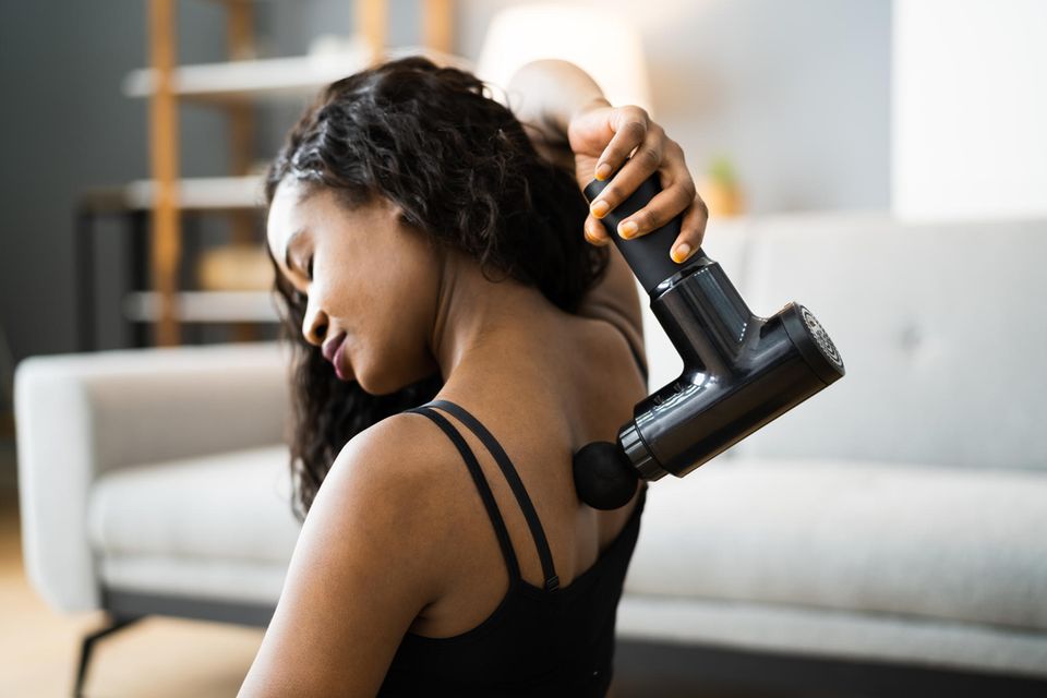 Massagepistole Test: Die besten 6 Modelle, Frau benutzt eine Massagepistole am Nacken