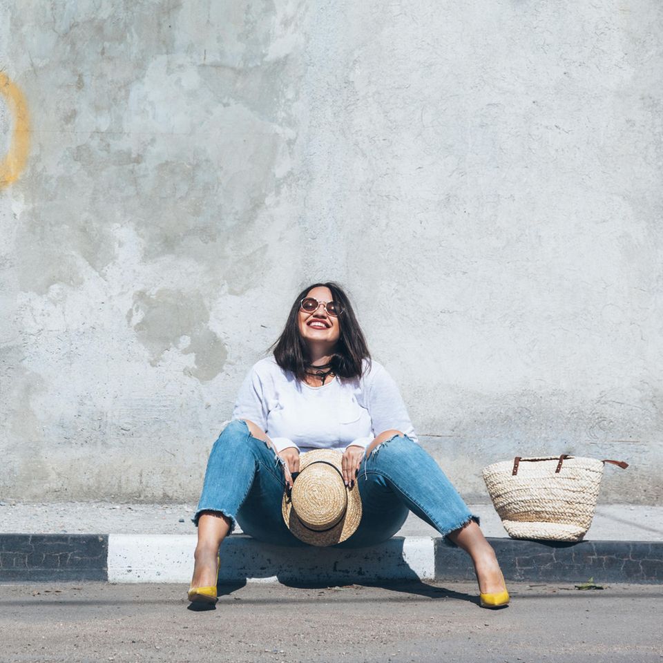 Mode-Einzelstück: Frau sitzt glücklich auf der Bordsteinkante