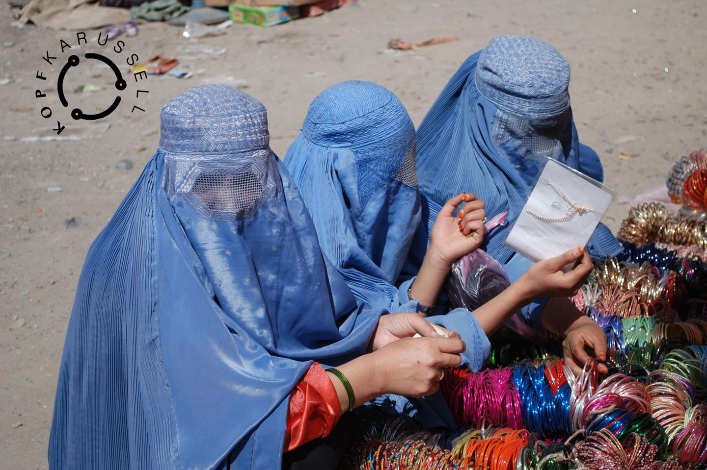 drei afghanische Frauen in traditionellen blauen Burkas schauen sich Armreifen an