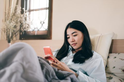 Ein Frau sitzt im Bett und schaut in ihr Smartphone.