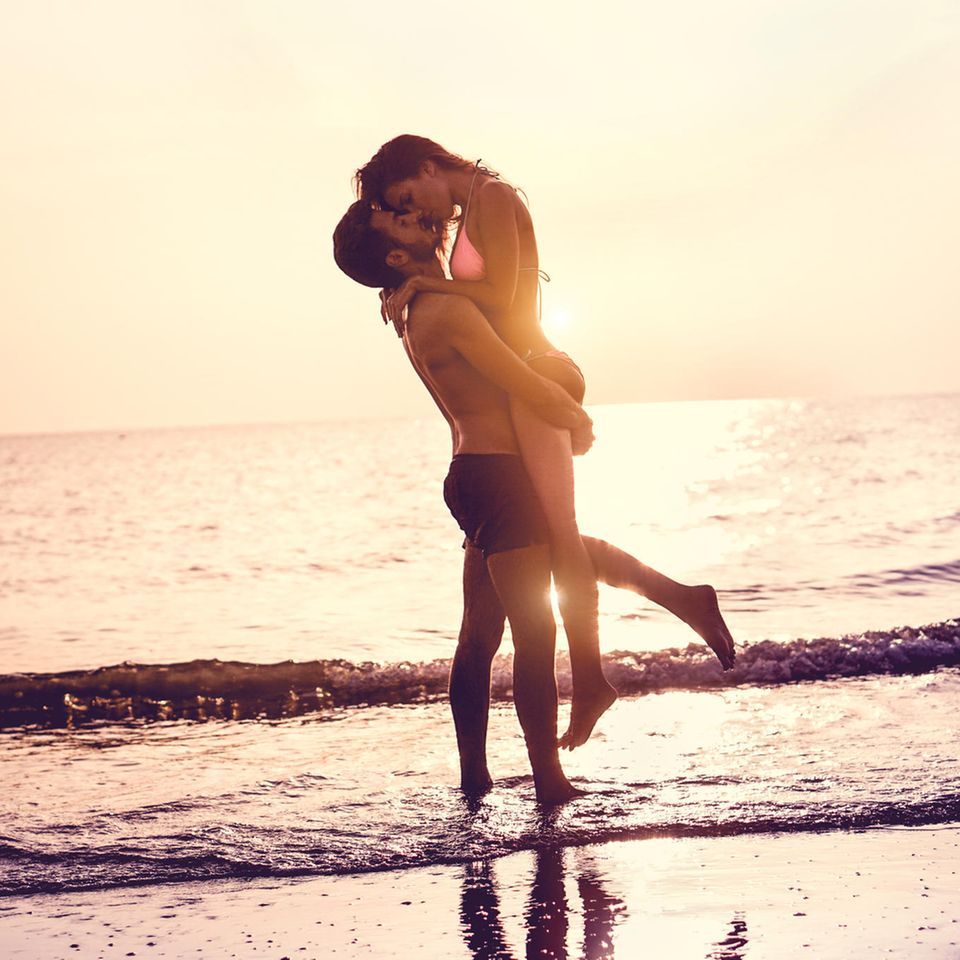 Sex im Urlaub: Mann hebt Frau am Strand hoch und küsst sie