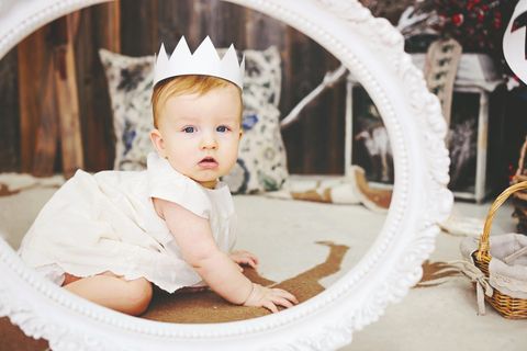 Ein Baby hat eine Krone auf sitzt in einem runden Rahmen und schaut in die Kamera.