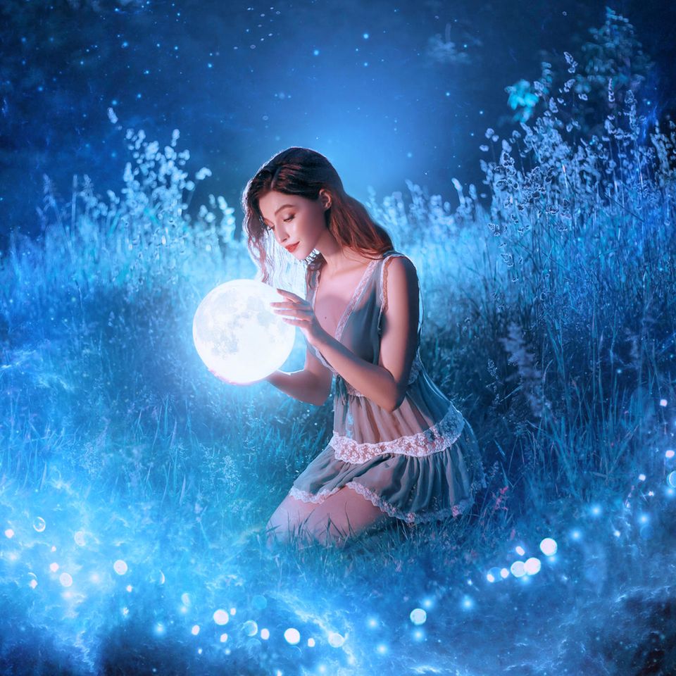 Horoskop: Frau im mystischen Sternenlicht hält blauen Planeten vor sich