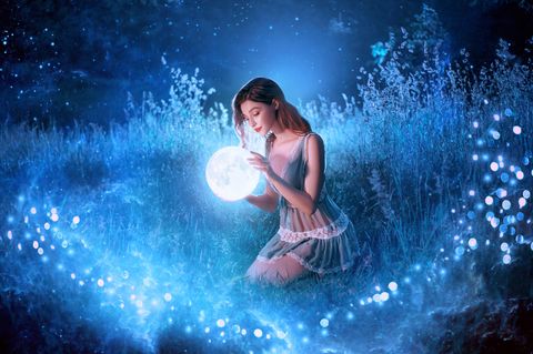 Horoskop: Frau im mystischen Sternenlicht hält blauen Planeten vor sich