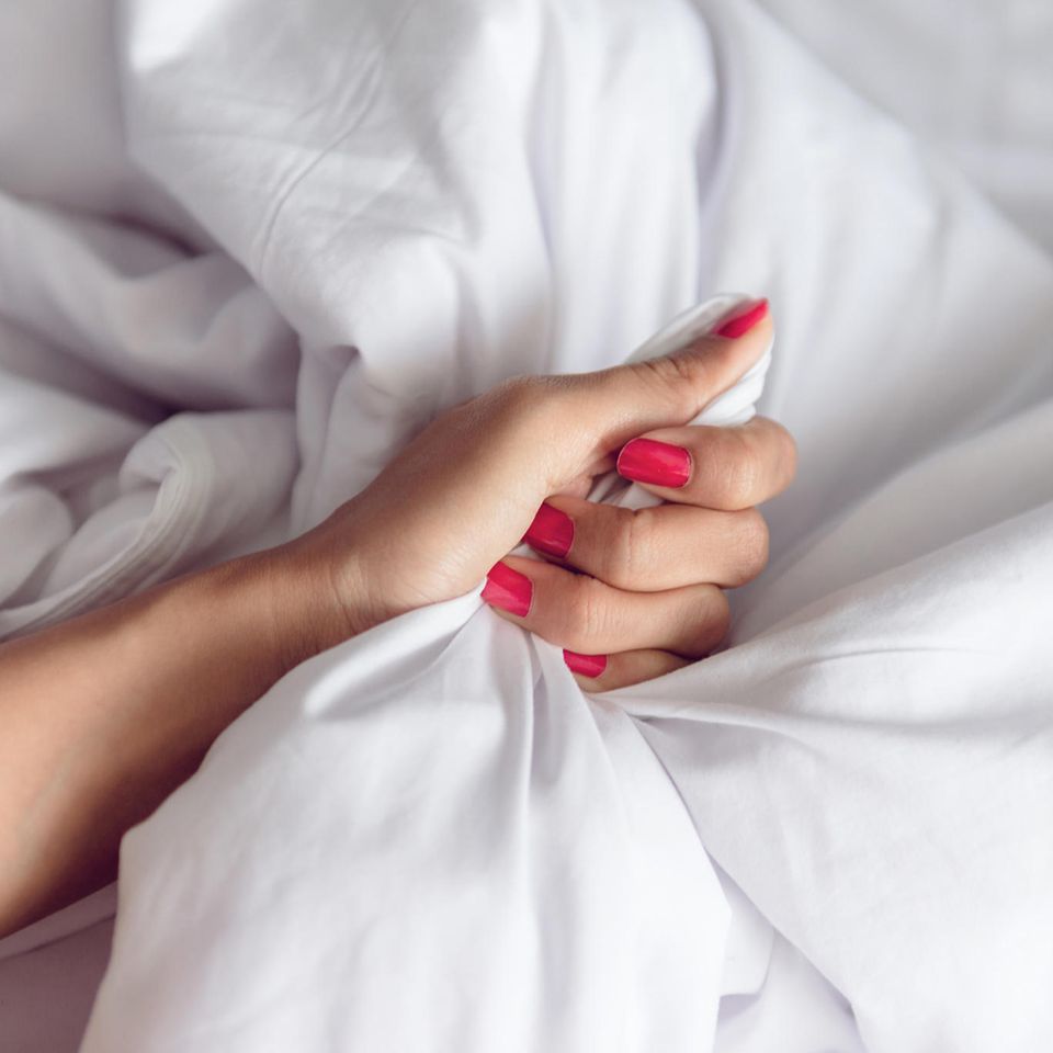 Vibrator mit Fernbedienung: Die besten Modelle, Frauenhand greift in Bettdecke