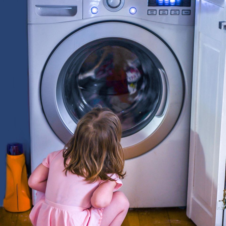 Ein Kind sitzt vor der Waschmaschine und wartet bis sie fertig ist.