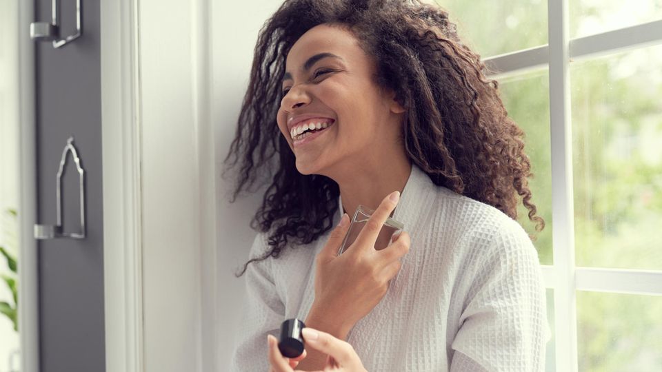 Parfum und Persönlichkeit: Das sagt dein Lieblingsduft über dich aus Parfum und Persönlichkeit: Frau lacht und hält ihren Lieblingsduft in der Hand