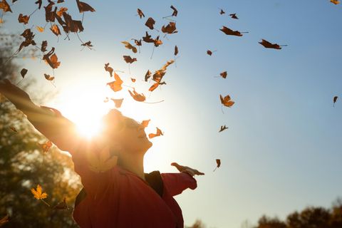 Frau wirft Herbstlaub in Luft