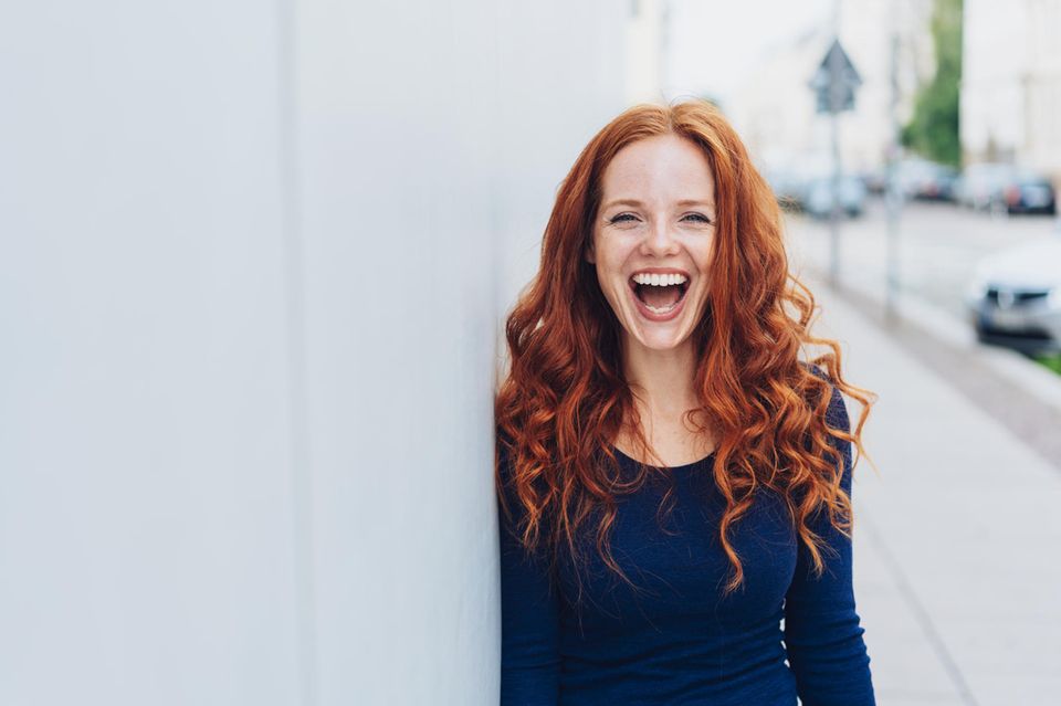 Horoskop: Rothaarige Frau lacht glücklich in die Kamera