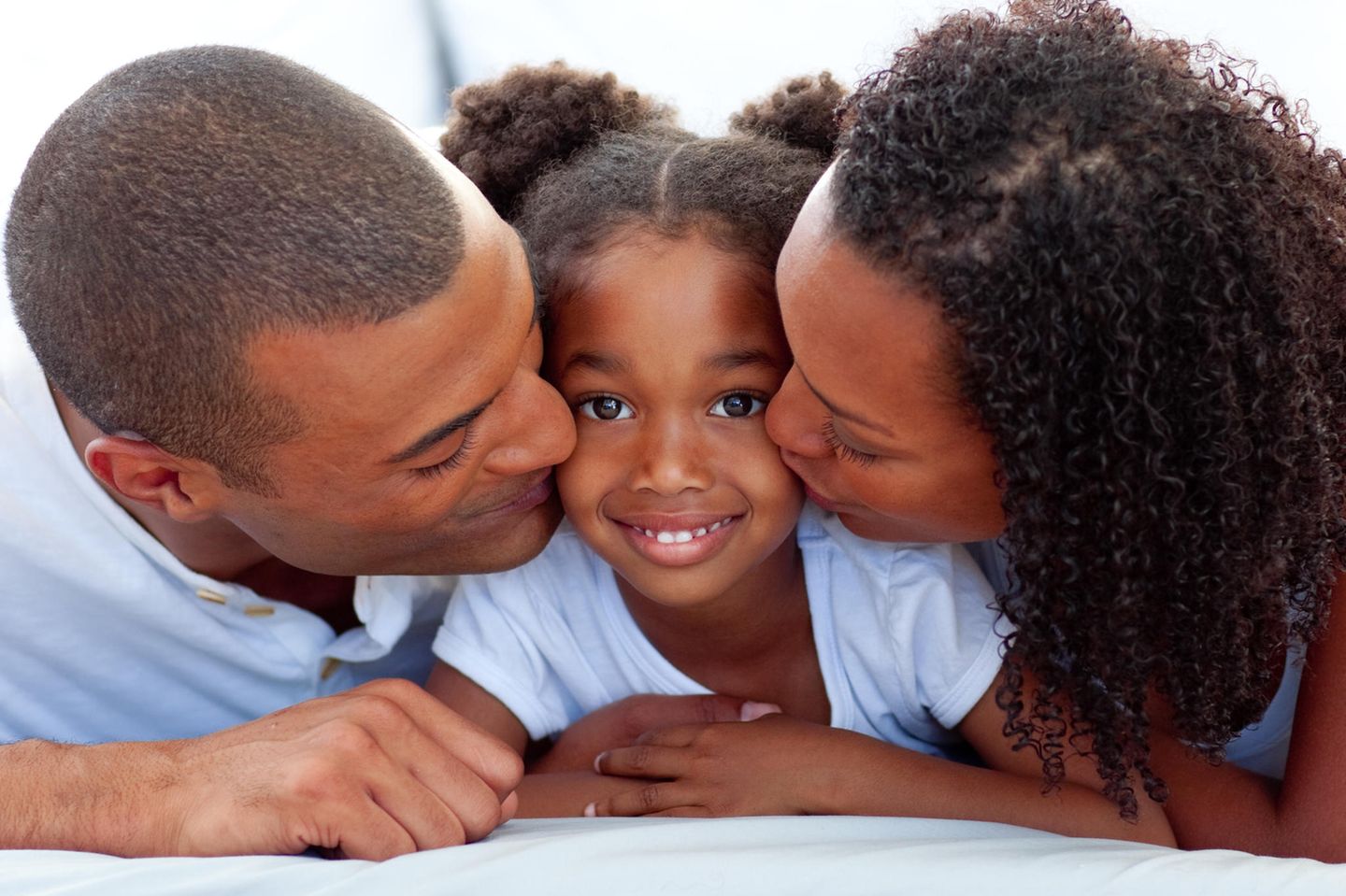 Kinder gegen Rassismus stark machen: Mutter und Vater küssen ihre Tochter auf die Wange