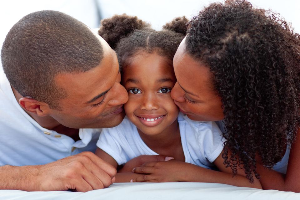 Kinder gegen Rassismus stark machen: Mutter und Vater küssen ihre Tochter auf die Wange