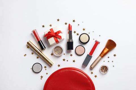 Vor einem Make-up Täschchen liegen Make-up-Produkte, ein Geschenk und Sternchen Dekoration.