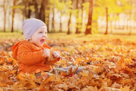 Ein Kind sitzt in einem Blätterhaufen und ist fröhlich.
