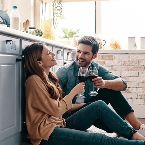Eine Frau und ein Mann sitzen glücklich in der Küche und stoßen mit Wein an