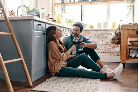 Eine Frau und ein Mann sitzen glücklich in der Küche und stoßen mit Wein an