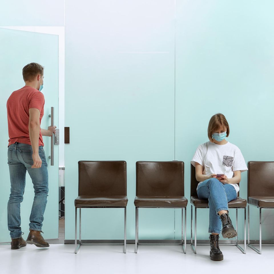 Eine Frau wartet im Wartezimmer eines Arztes, während ein Mann bereits aufgerufen wurde
