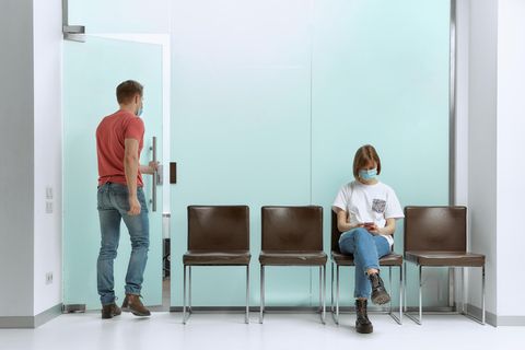 Eine Frau wartet im Wartezimmer eines Arztes, während ein Mann bereits aufgerufen wurde