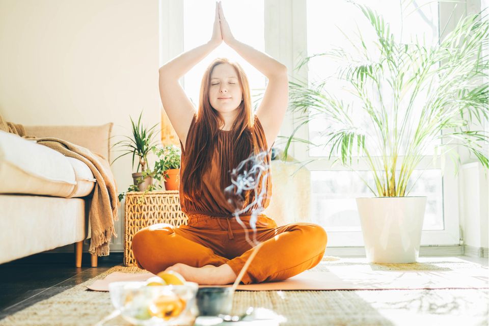 Das sind die 5 größten Mythen über Yoga: Frau übt zu Hause Yoga mit Räucherstäbchen.