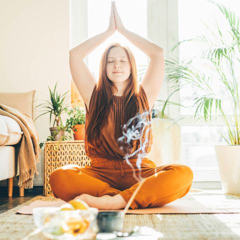 Das sind die 5 größten Mythen über Yoga: Frau übt zu Hause Yoga mit Räucherstäbchen.