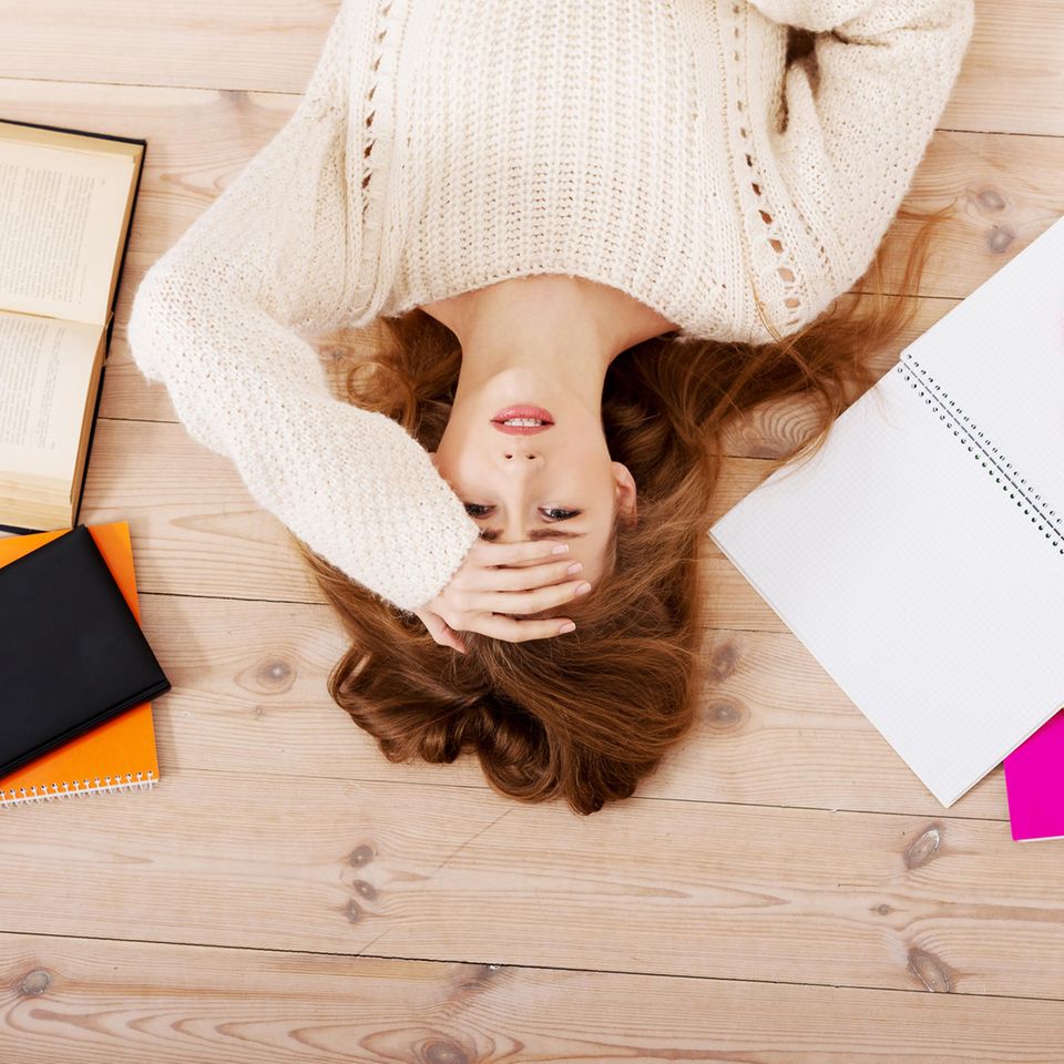 Stress-Gefühle: Junge Frau liegt auf dem Boden umgeben von Lernmaterial