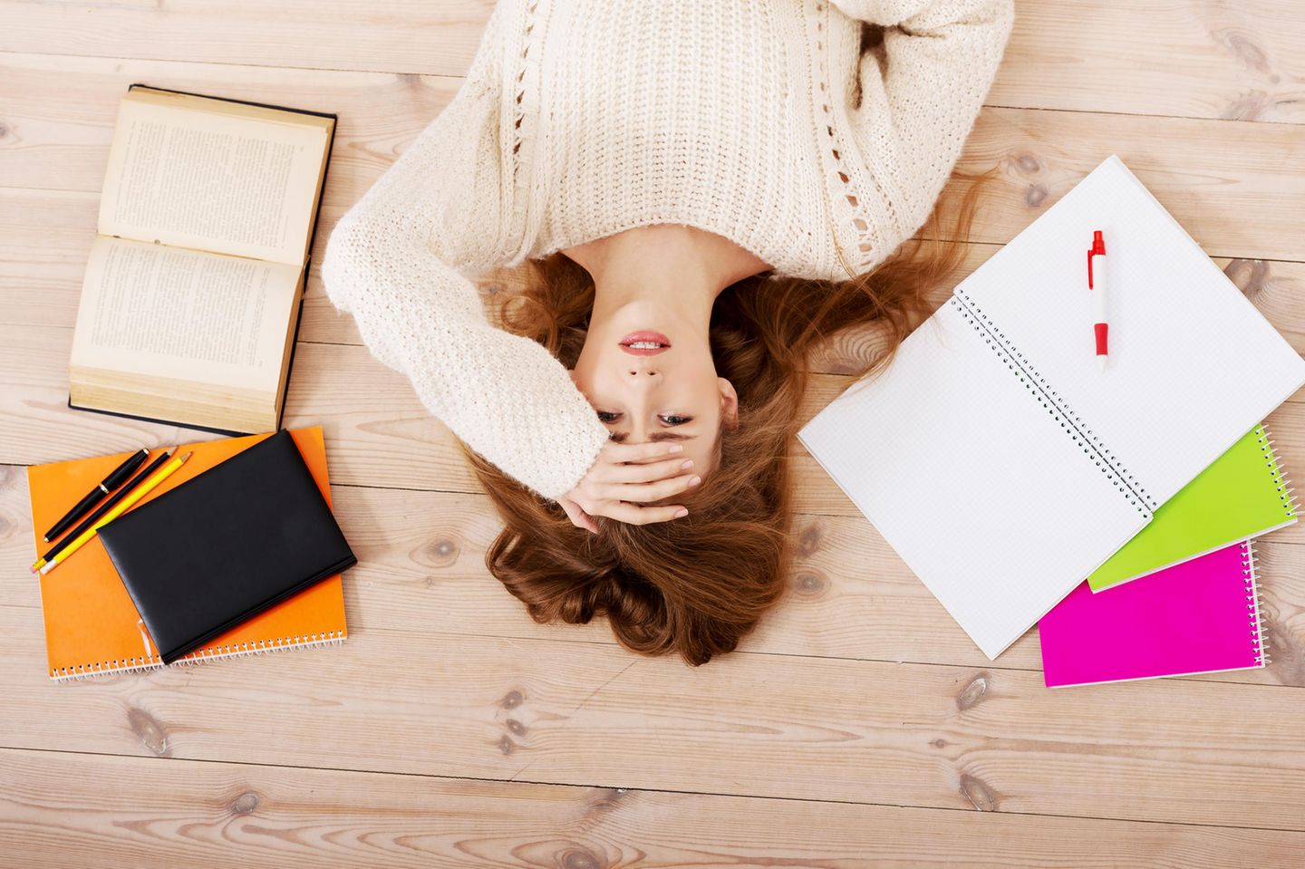 Stress-Gefühle: Junge Frau liegt auf dem Boden umgeben von Lernmaterial