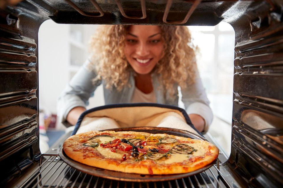 Eine Frau nimmt eine Pizza aus dem Ofen.