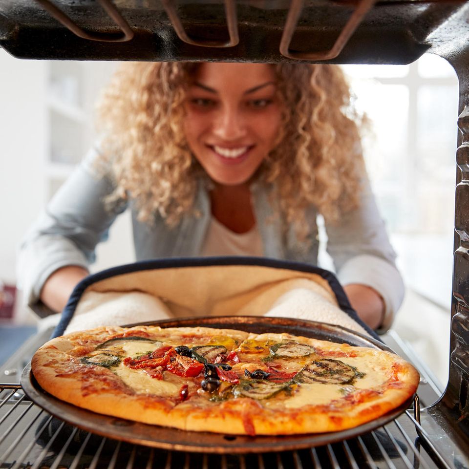 Eine Frau nimmt eine Pizza aus dem Ofen.