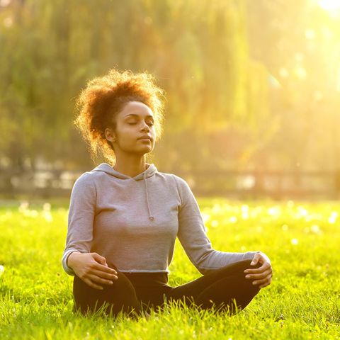 3 Missverständnisse über Meditation – und wie es wirklich ist: Frau meditiert draußen auf einer Wiese.