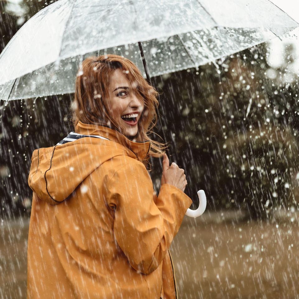 Was sagt deine Lieblings-Jahreszeit über dich aus? Frau lacht glücklich im Regen.