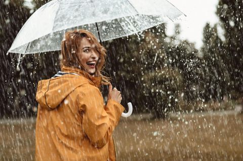 Was sagt deine Lieblings-Jahreszeit über dich aus? Frau lacht glücklich im Regen.
