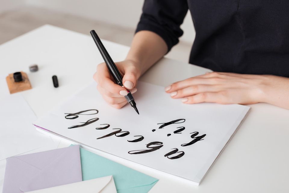 Eine Frau malt verschiedene Buchstaben im Handlettering Stil