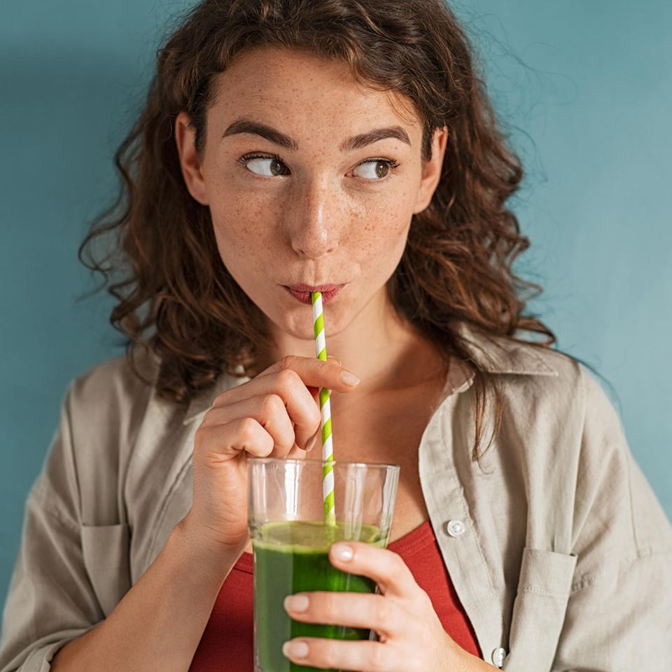 Eine Frau trinkt einen grünen Saft mit einem Strohhalm.