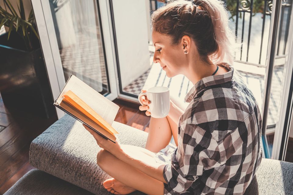 Frau liest Buch und trinkt Tee: Macht Minimalismus uns wirklich glücklicher?