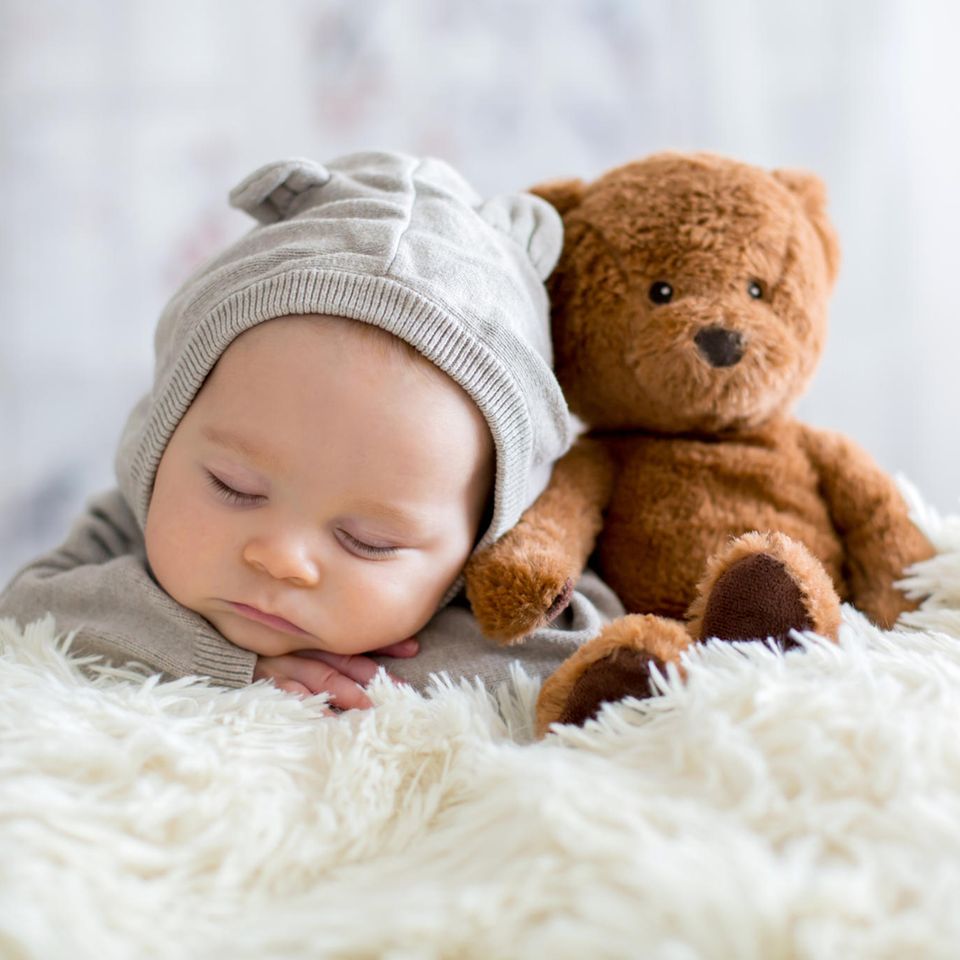 Ein Neugeborenes schläft neben einem Teddy.