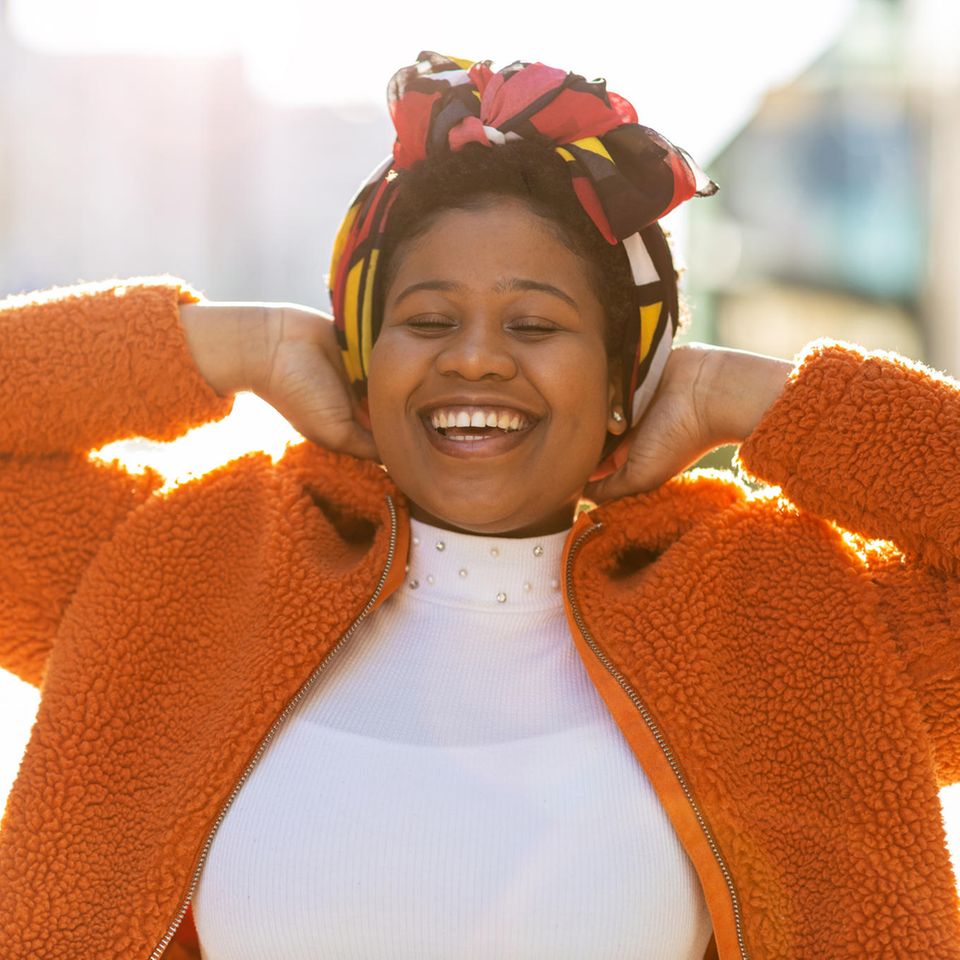 Fröhliche Frau in orangefarbener Jacke: 8 Gewohnheiten, die erfolgreiche Menschen jeden Tag pflegen