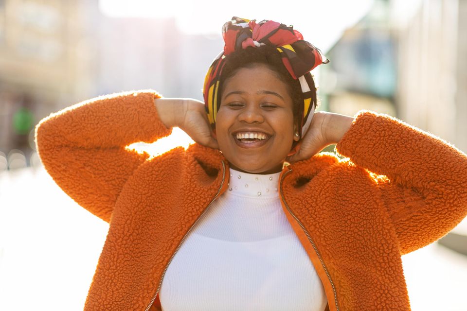 Fröhliche Frau in orangefarbener Jacke: 8 Gewohnheiten, die erfolgreiche Menschen jeden Tag pflegen