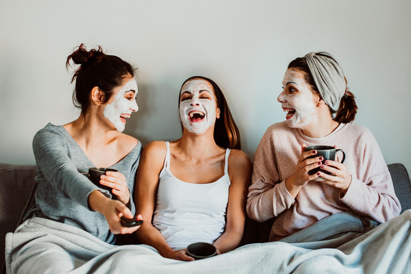 Zwei Frauen liegen lachend mit Gesichtsmasken im Bett.