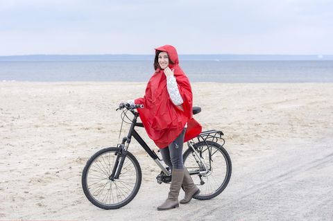 Regenponcho fürs Fahrrad: Diese 6 Modelle halten dich sicher trocken, Frau, Fahrrad, roter Regenponcho, Strand