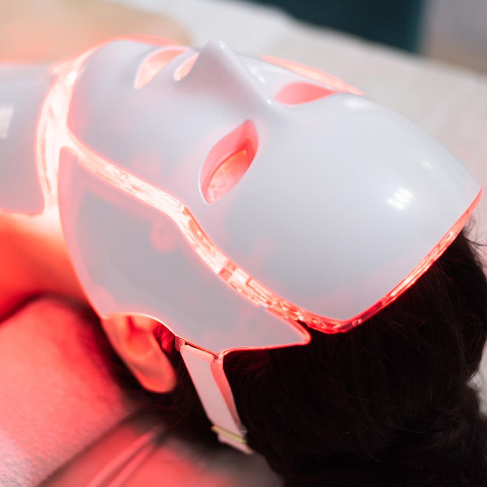Frau liegt auf Bett mit LED-Maske im Gesicht