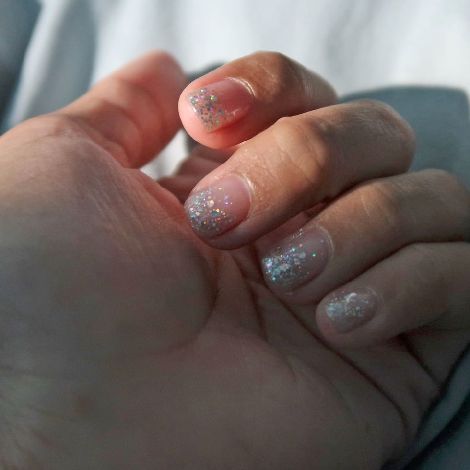 Die Hände einer Frau, deren Nägel mit silbernem Nagellack lackiert sind