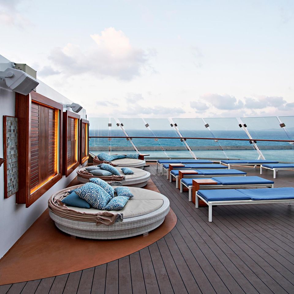 Trans-Reisen: Das Deck eines Kreuzfahrtschiffs. Zu sehen sind blaue Liegen und ein brauner Holzfußboden. Im Hintergrund das Meer