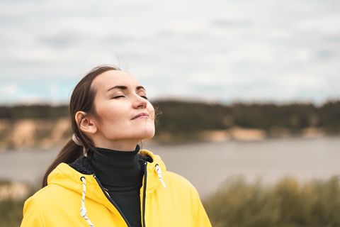 Schleimhaut der Atemwege: eine Frau mit Pferdeschwanz und gelber Regenjacke streckt mit geschlossenen Augen die Nase in den Wind