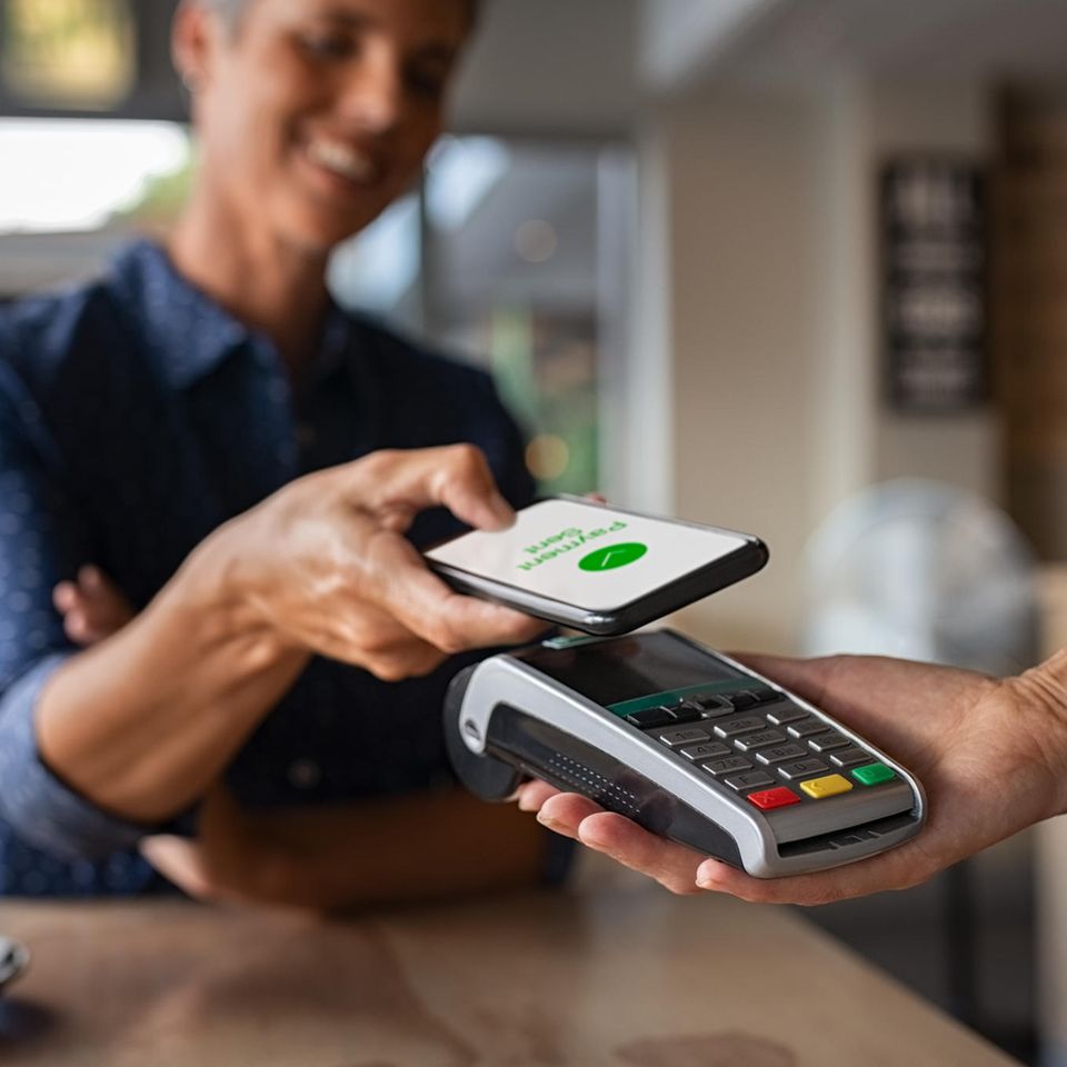 Bezahlen mit Bargeld: eine Frau legt ihr Handy auf ein Kartenlesegerät um zu bezahlen.