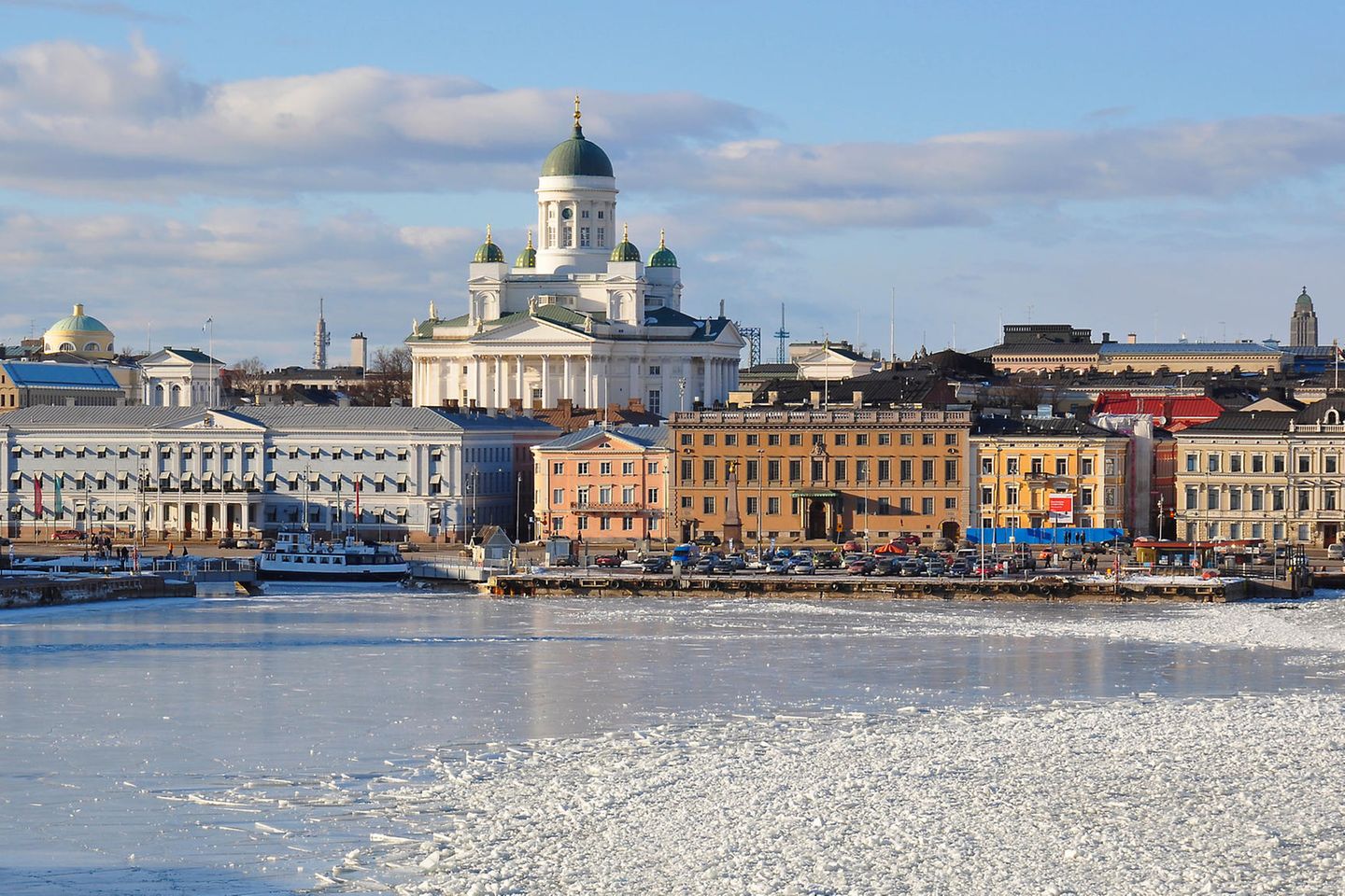 Helsinki: Die Skyline Helsinkis. Das Wasser ist gefroren und mit Schnee bedeckt. Der Himmel ist hellblau mit grauen Wolken