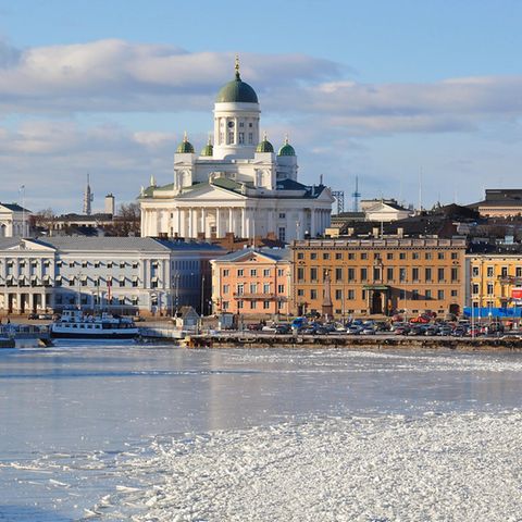 Helsinki: Die Skyline Helsinkis. Das Wasser ist gefroren und mit Schnee bedeckt. Der Himmel ist hellblau mit grauen Wolken