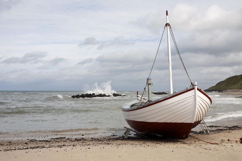 Jütland: ein kleines weißes Holzboot liegt an einem Strand, vor einem dunklen Meer mit grauem Himmel